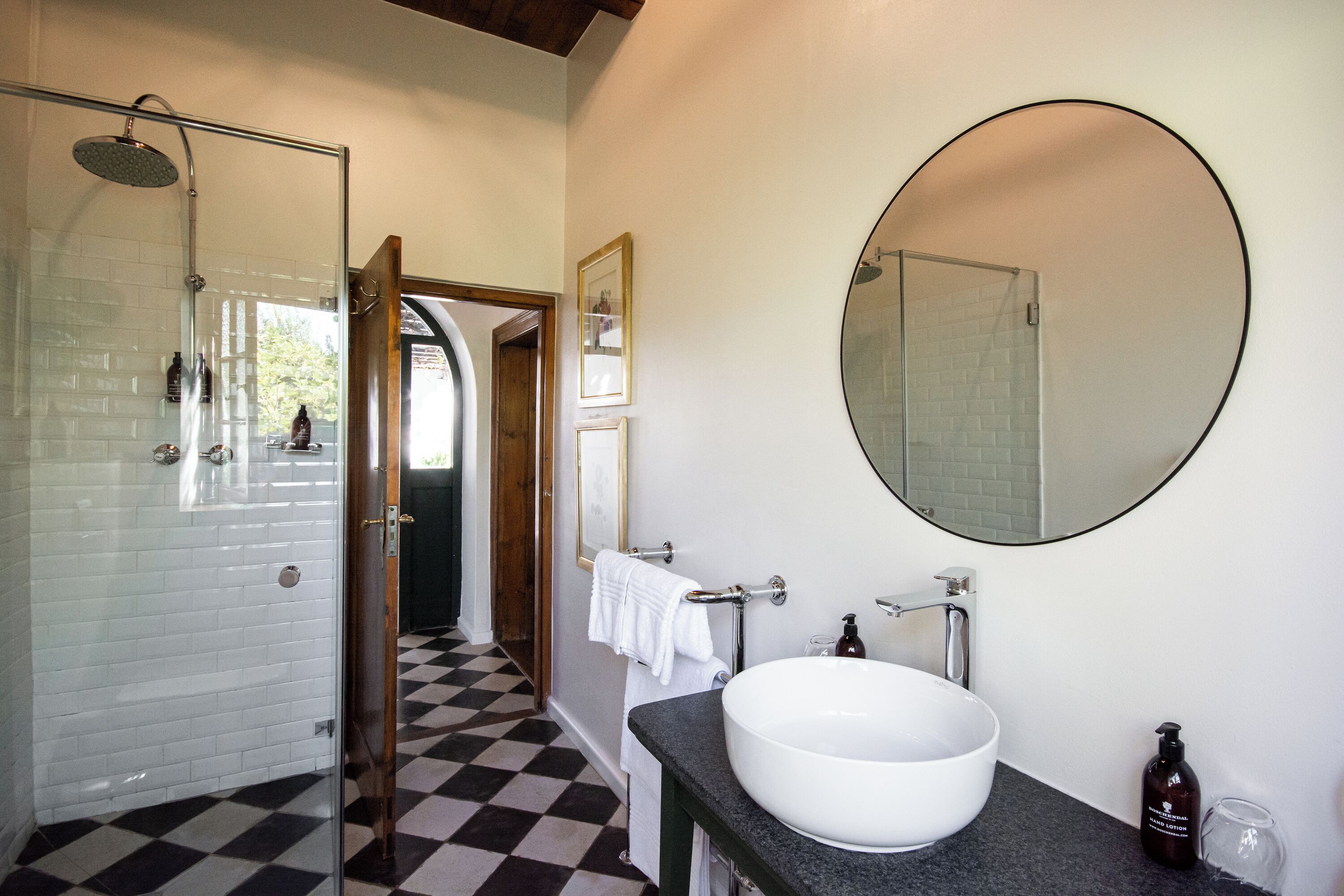 A bathroom with a checkered floor, a white sink, a large mirror, and a shower with a glass door.