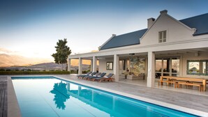 A modern house with a swimming pool, outdoor seating, and a view of mountains.