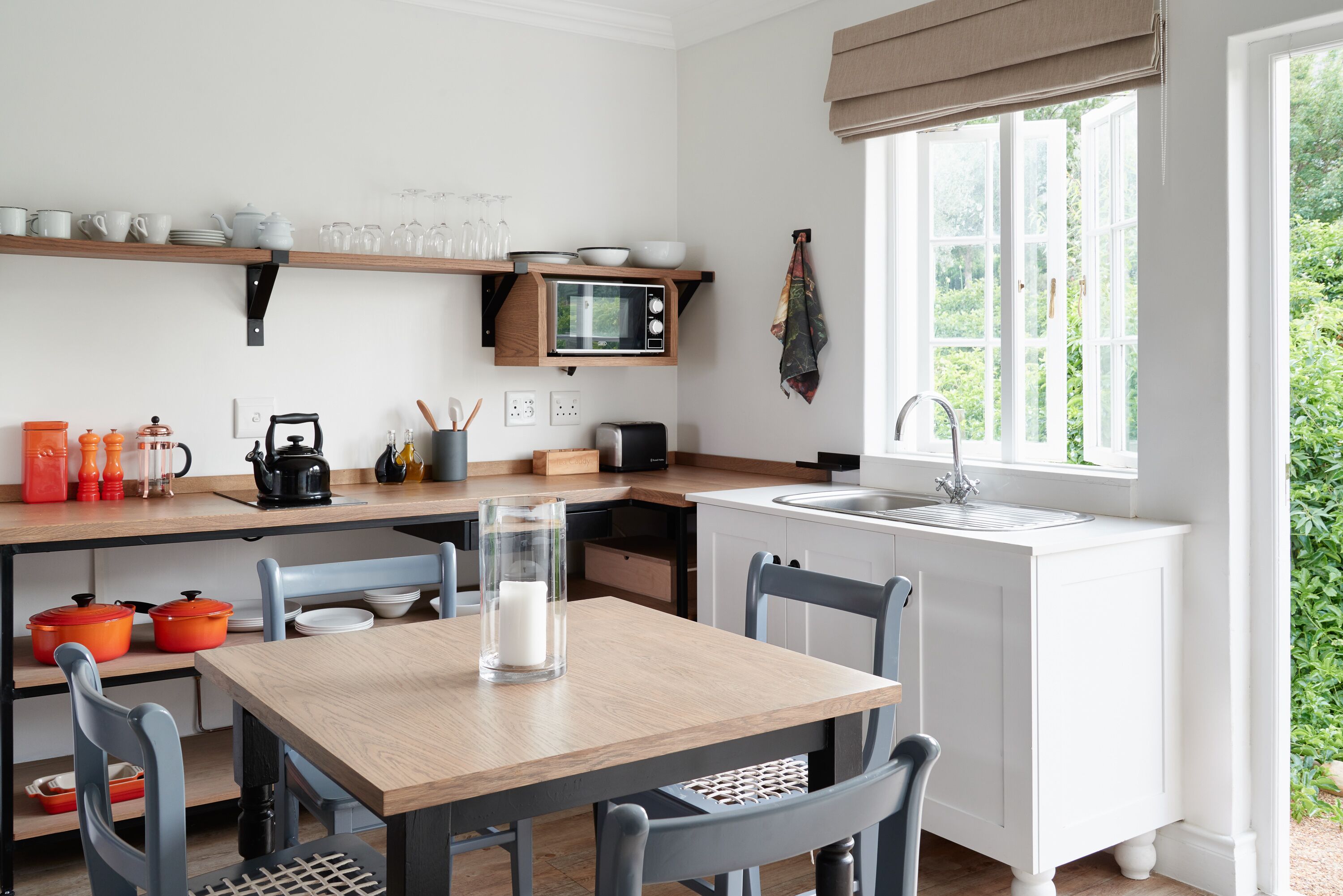 Una cocina compacta con una mesa de madera, sillas, un microondas y un lavamanos.