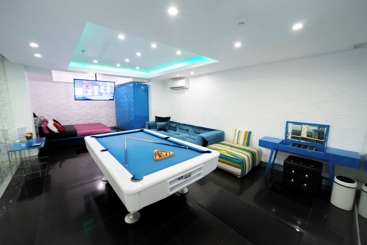 Un salon moderne avec une table de billard, un canapé, un téléviseur et un mur d’accent bleu.