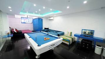 Una sala de estar moderna con una mesa de billar, un sofá, un televisor y una pared de acento azul.