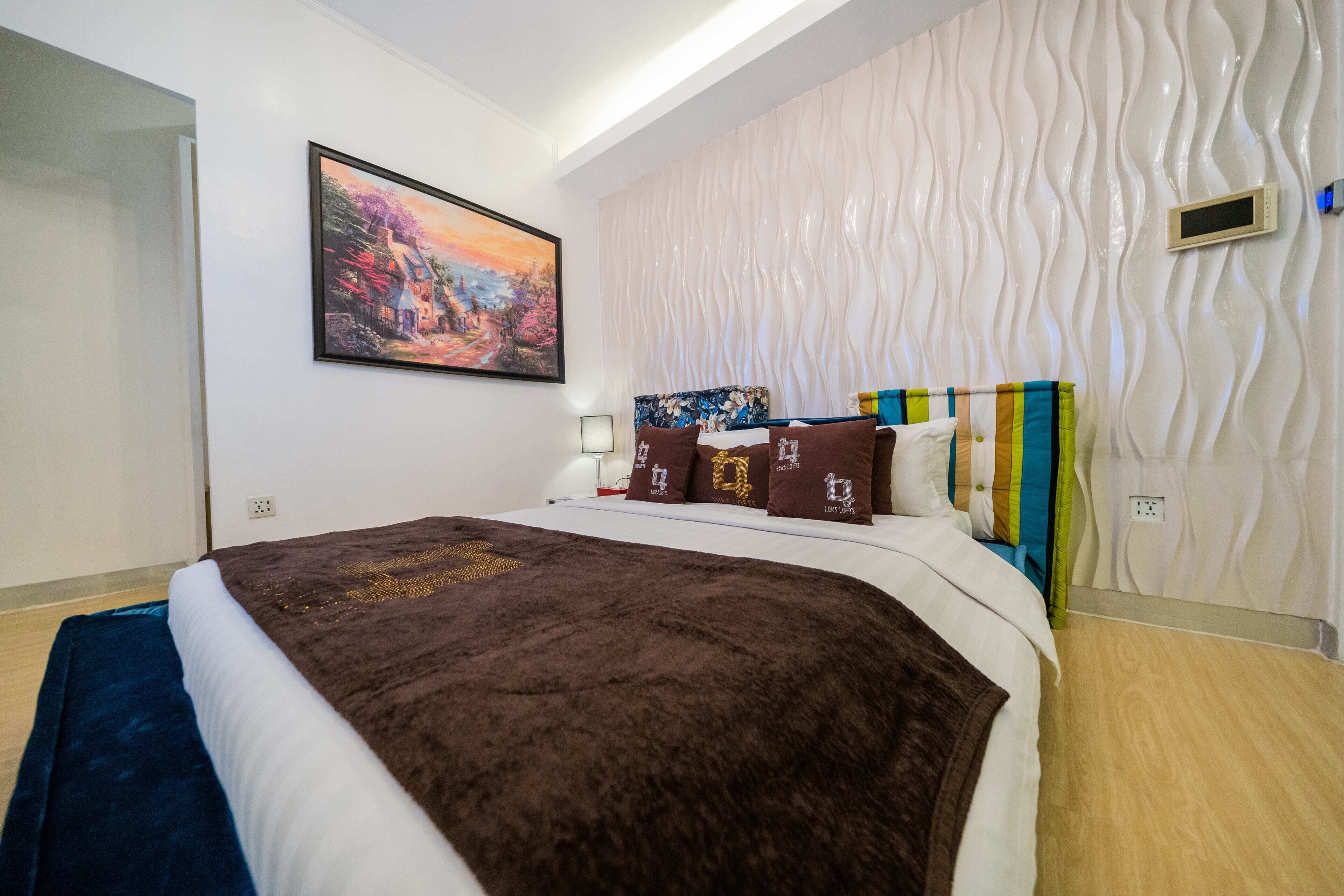 A modern bedroom with a large bed, a painting on the wall, and a textured wall design.