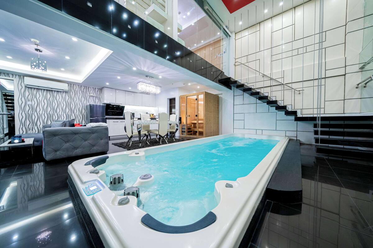 Une piscine intérieure moderne dotée d’un jacuzzi, d’un escalier et d’un coin repas offrant une vue sur la piscine.