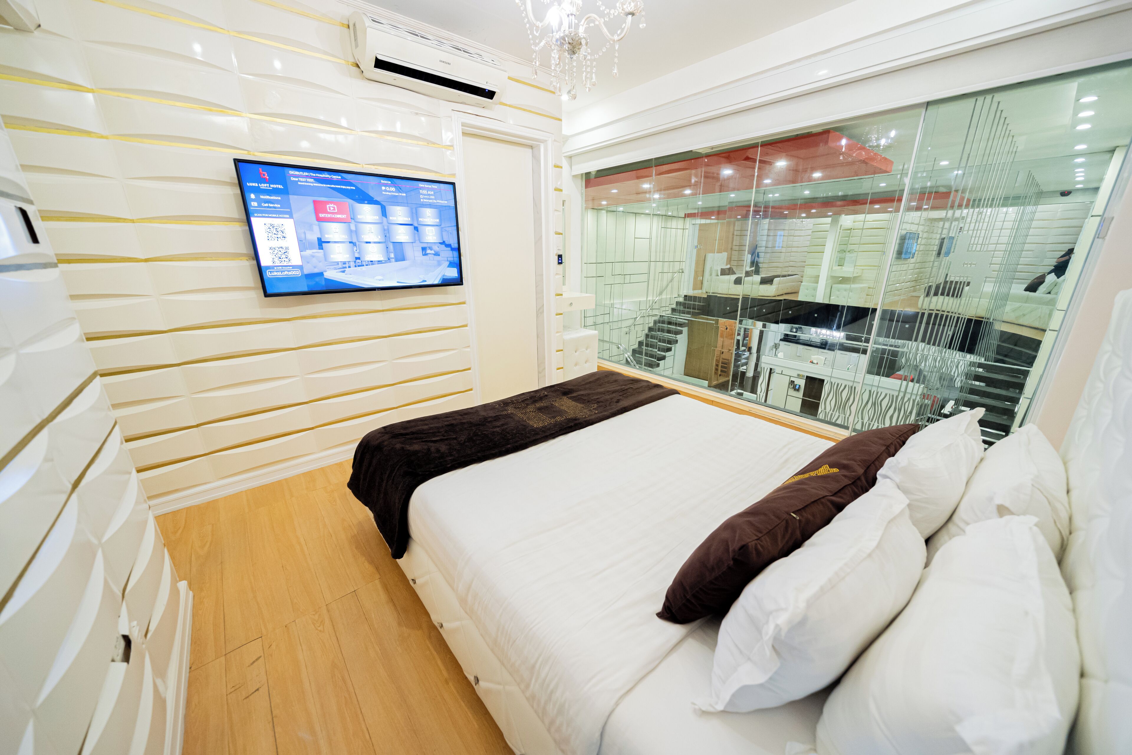 Habitación de hotel moderna con una cama grande, televisor montado y pared de vidrio con vista al interior.