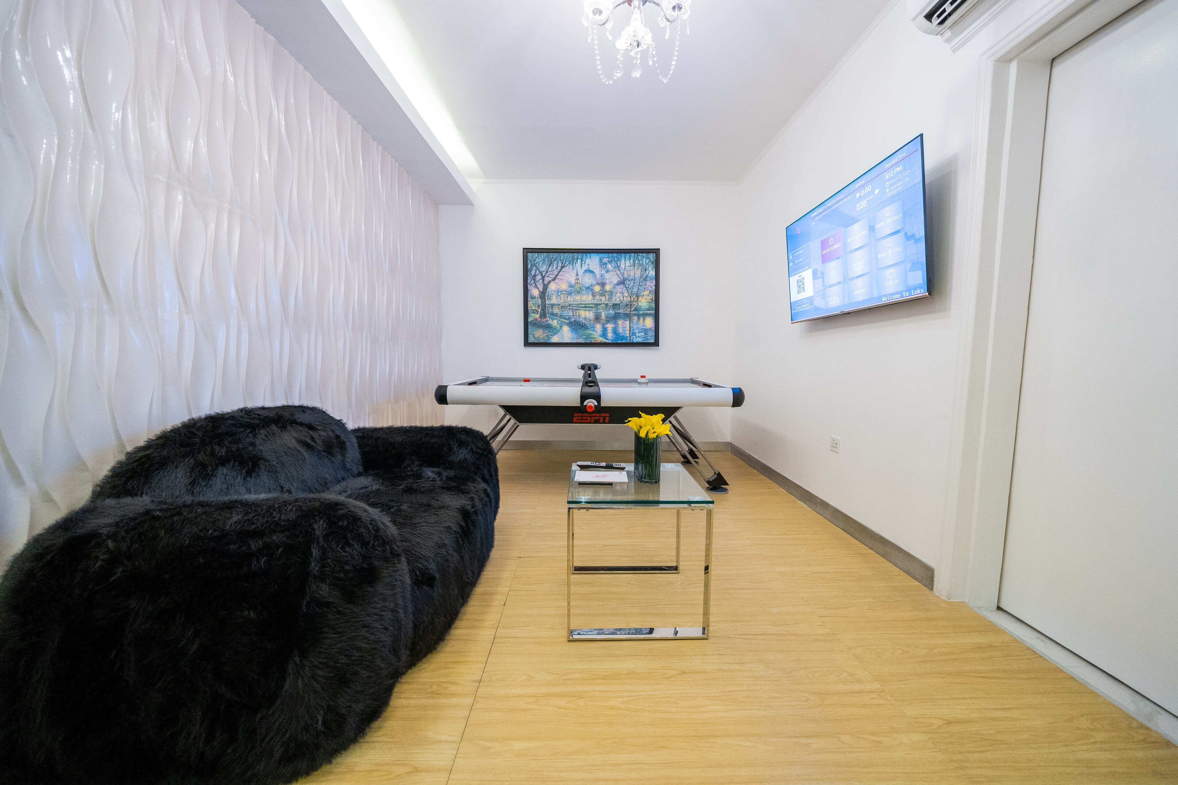 A room with a black fur sofa, a glass coffee table with a vase, a painting on the wall, and a television displaying a menu.