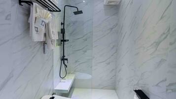 Un baño moderno con inodoro, ducha con cabezal de ducha de mano y toallero con toallas dobladas.