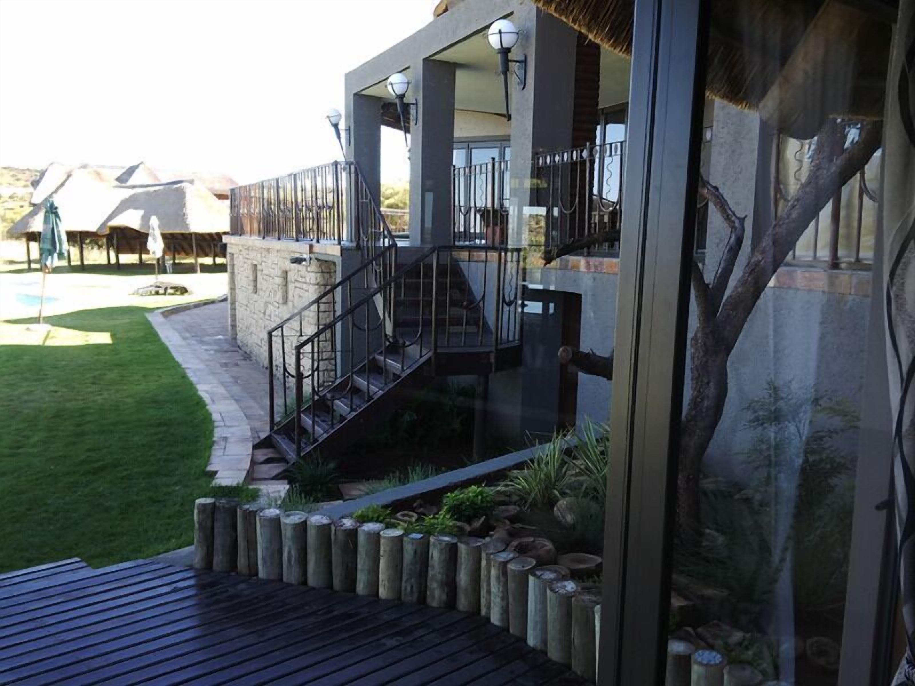 A modern building with a glass facade, a wooden deck, and a stone pathway leading to a staircase.