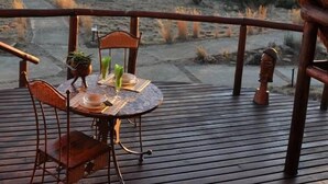 An outdoor dining area with a table and chairs, a thatched roof, and a view of a dry landscape.