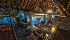 A spacious, multi-level interior with a high ceiling and exposed wooden beams. There is a seating area with couches and a coffee table, and a staircase connecting the levels.