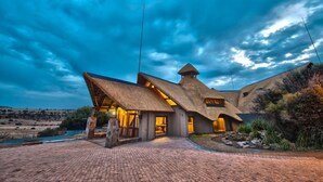A modern house with a unique thatched roof design, situated near a body of water.