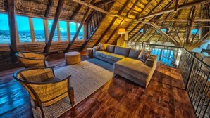A cozy, rustic room with a wooden ceiling and large windows overlooking a beach.