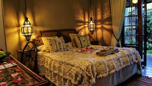 A room with a bed, two wall-mounted lanterns, a wooden headboard, and a view of greenery outside.