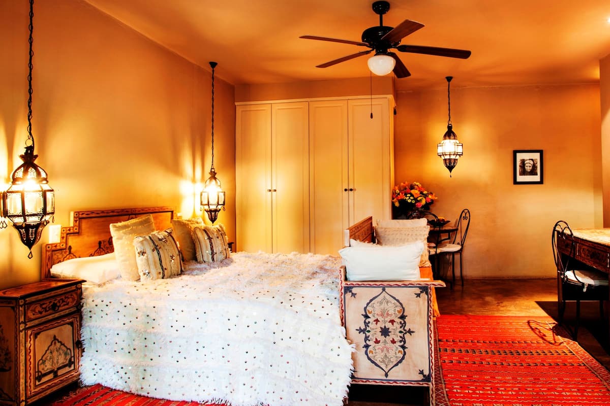 Un dormitorio con una cama, ventilador de techo, candelabro, cómoda, una silla y un escritorio.
