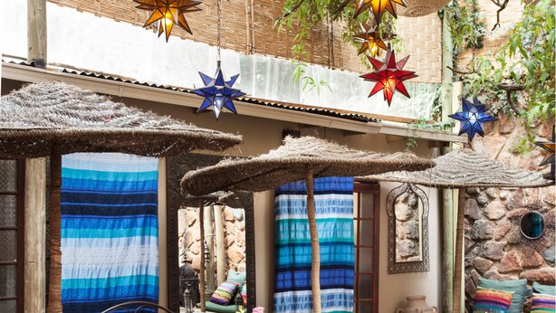 A cozy outdoor seating area with colorful striped cushions, a wooden table, and hanging star-shaped lanterns.