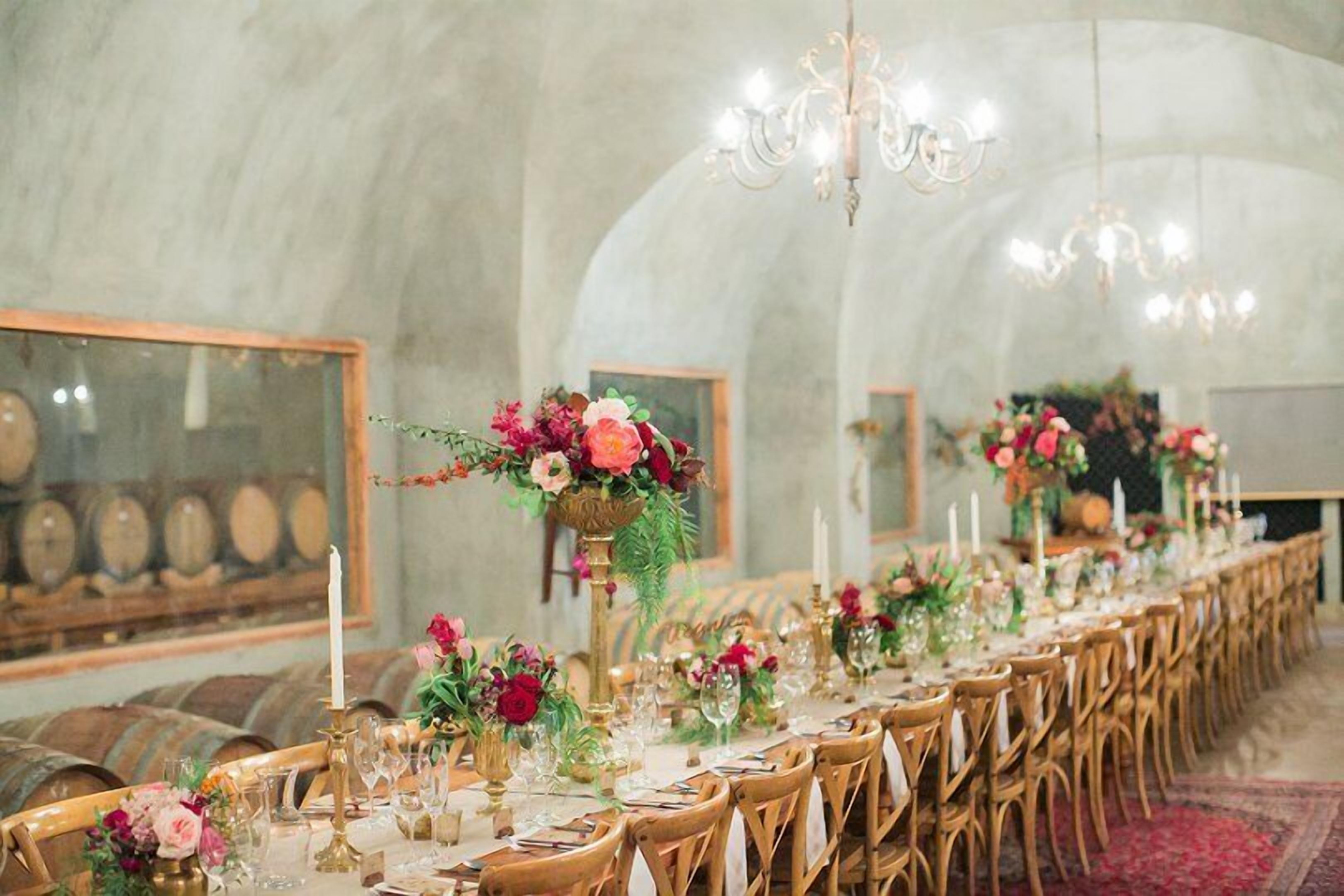 A long dining table set with chairs, decorated with floral centerpieces and candles, in a room with arched ceilings and chandeliers.