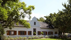 A white building with a thatched roof, surrounded by a well-maintained garden with hay bales and potted plants. - Montpellier De Tulbagh (Tulbagh)