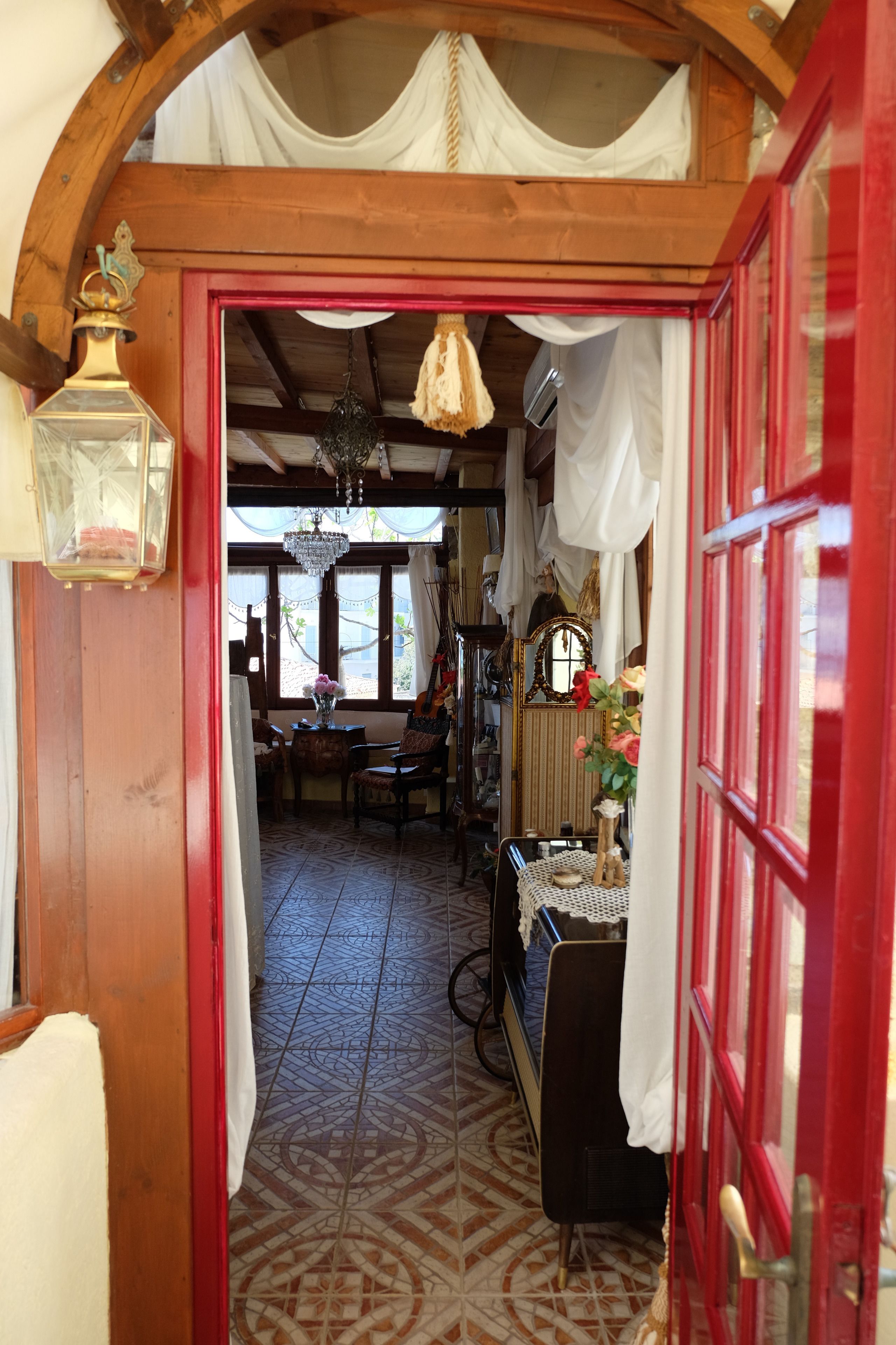 A narrow hallway with patterned floor tiles, a wooden door frame, and a red door.