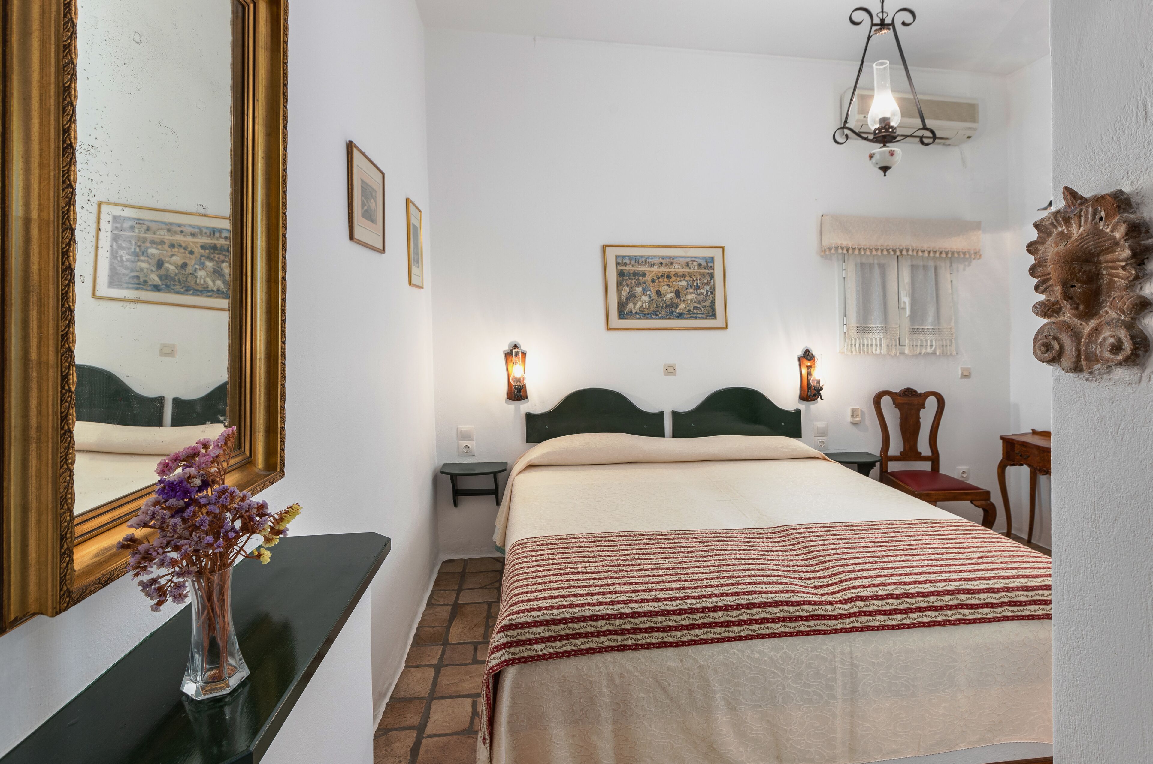 A neatly arranged bedroom with a large bed, a bedside table, a mirror, and a wall-mounted lamp.