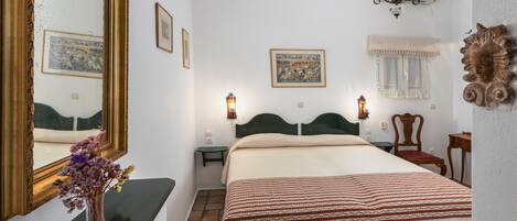 A neatly arranged bedroom with a large bed, a bedside table, a mirror, and a wall-mounted lamp.