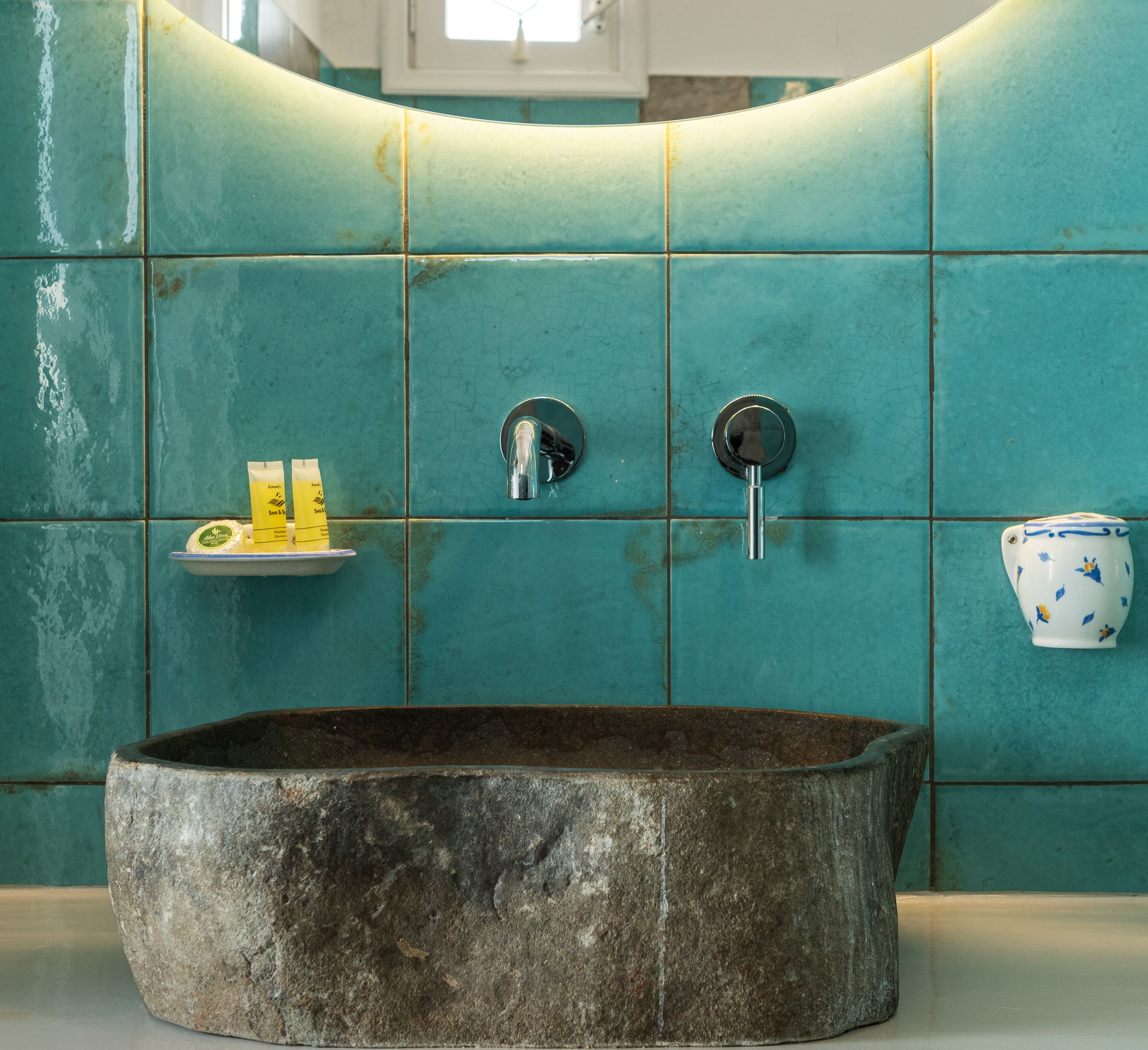 Une salle de bain avec des carreaux de couleur turquoise, un lavabo en pierre et une petite étagère contenant des articles de toilette.
