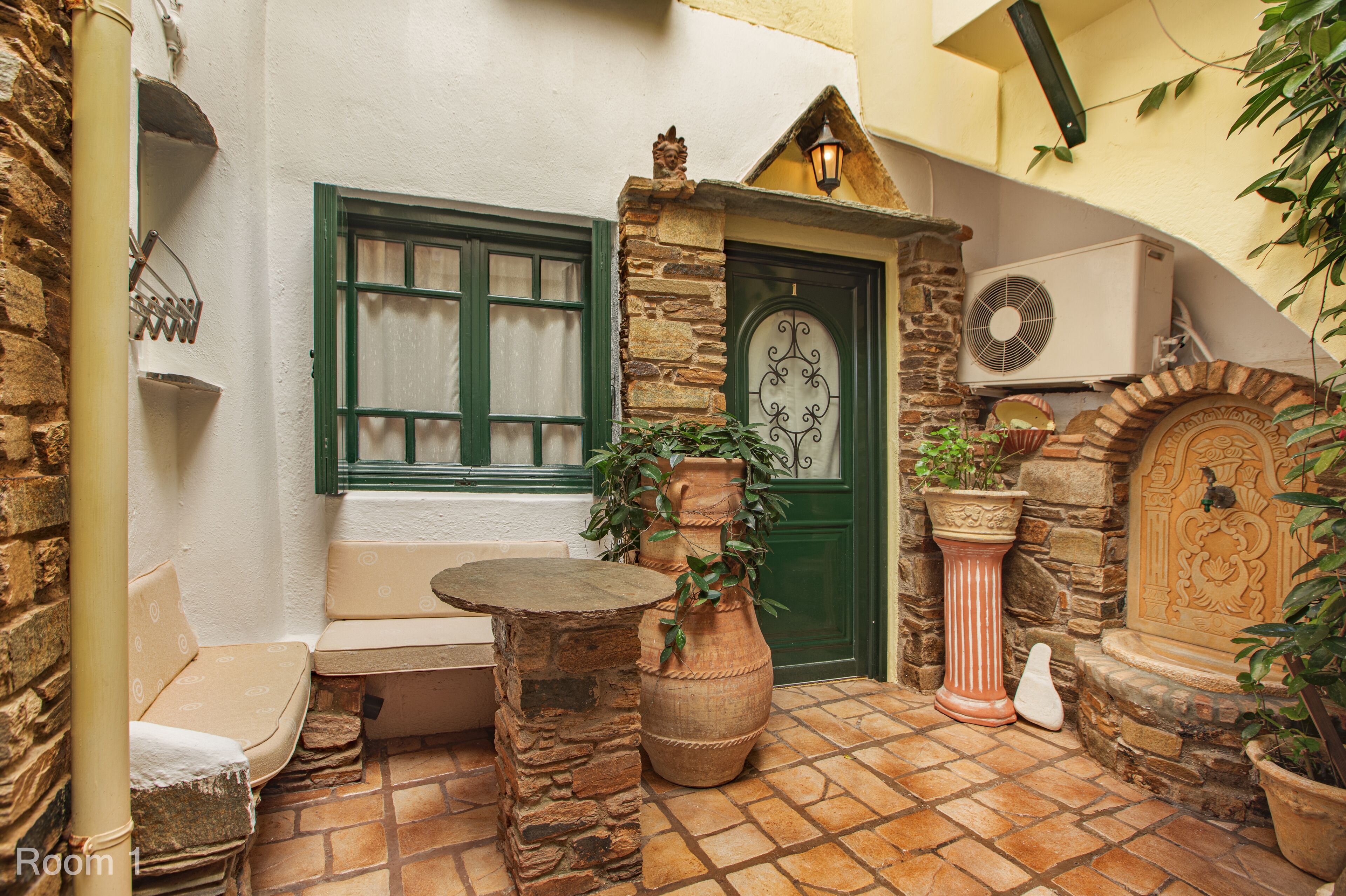 A cozy courtyard with a stone bench, a potted plant, and a door with a decorative metalwork design.