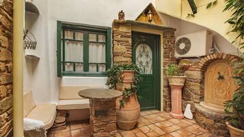 A cozy courtyard with a stone bench, a potted plant, and a door with a decorative metalwork design.