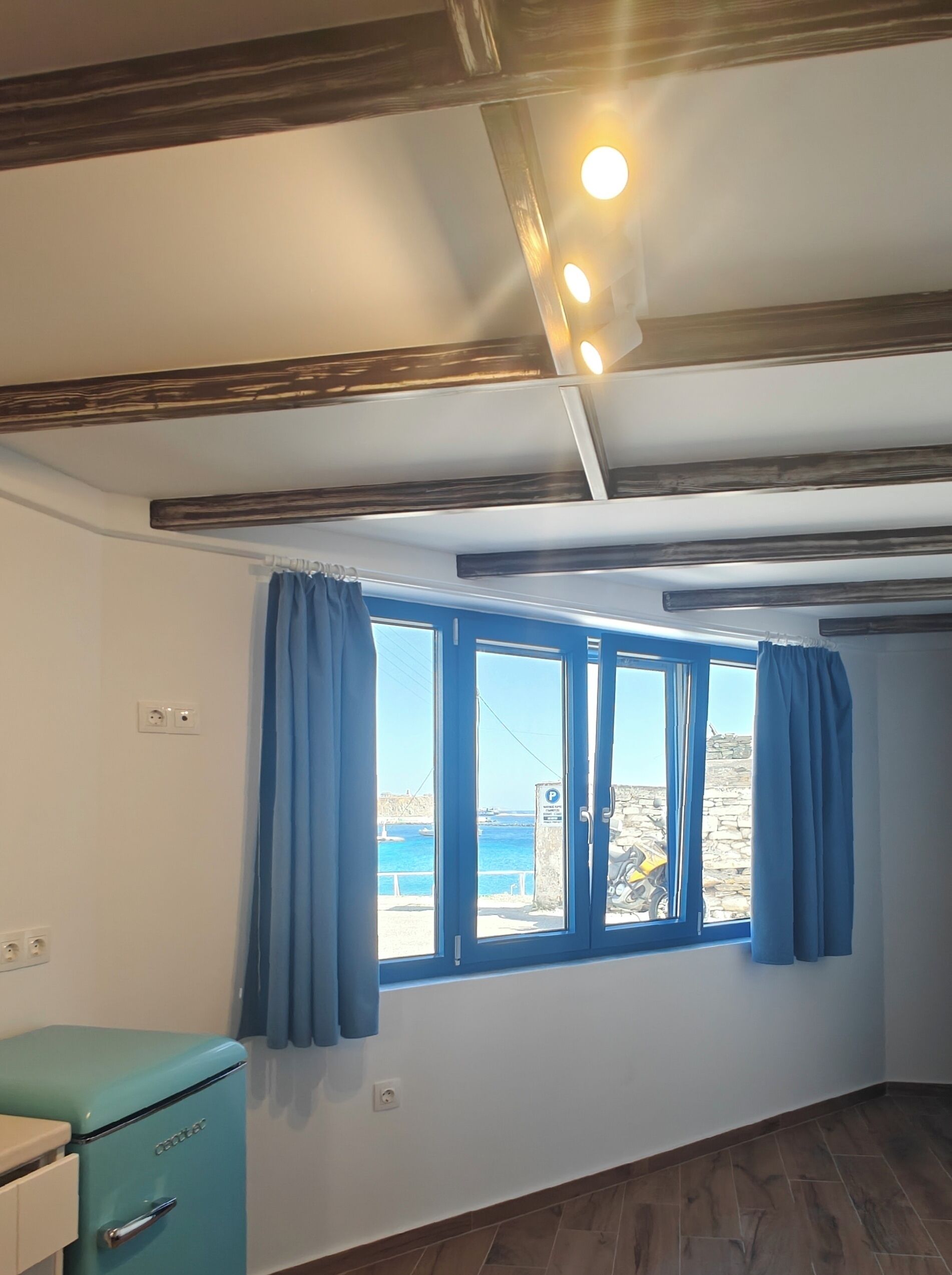 A room with a large window, a vintage-style refrigerator, and a ceiling with exposed beams and recessed lighting.