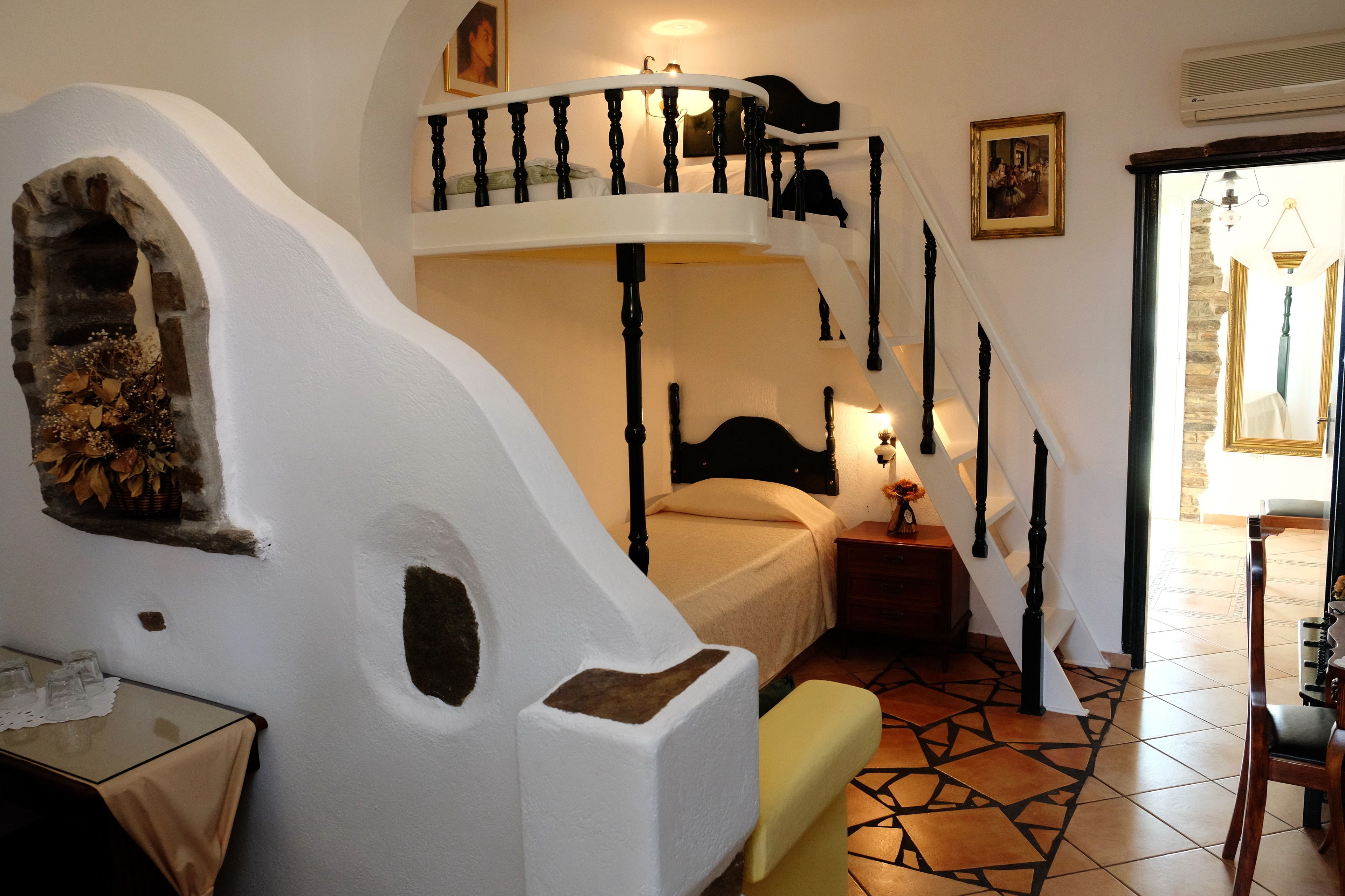 Een slaapkamer met een bed, nachtkastje, stoel, trap en een klein balkon.