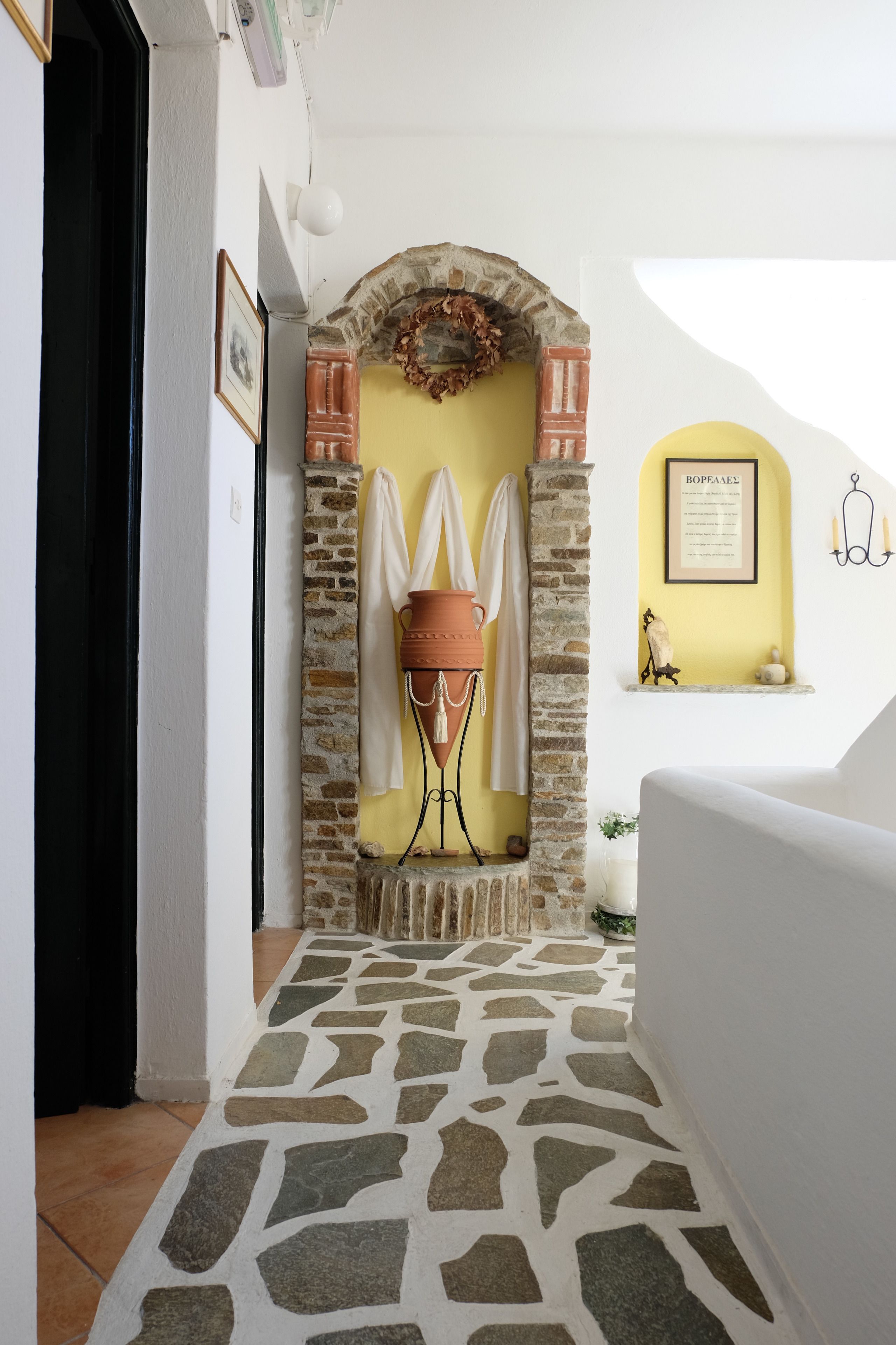 A hallway with a stone floor, a brick fireplace, and a yellow wall with a framed certificate.
