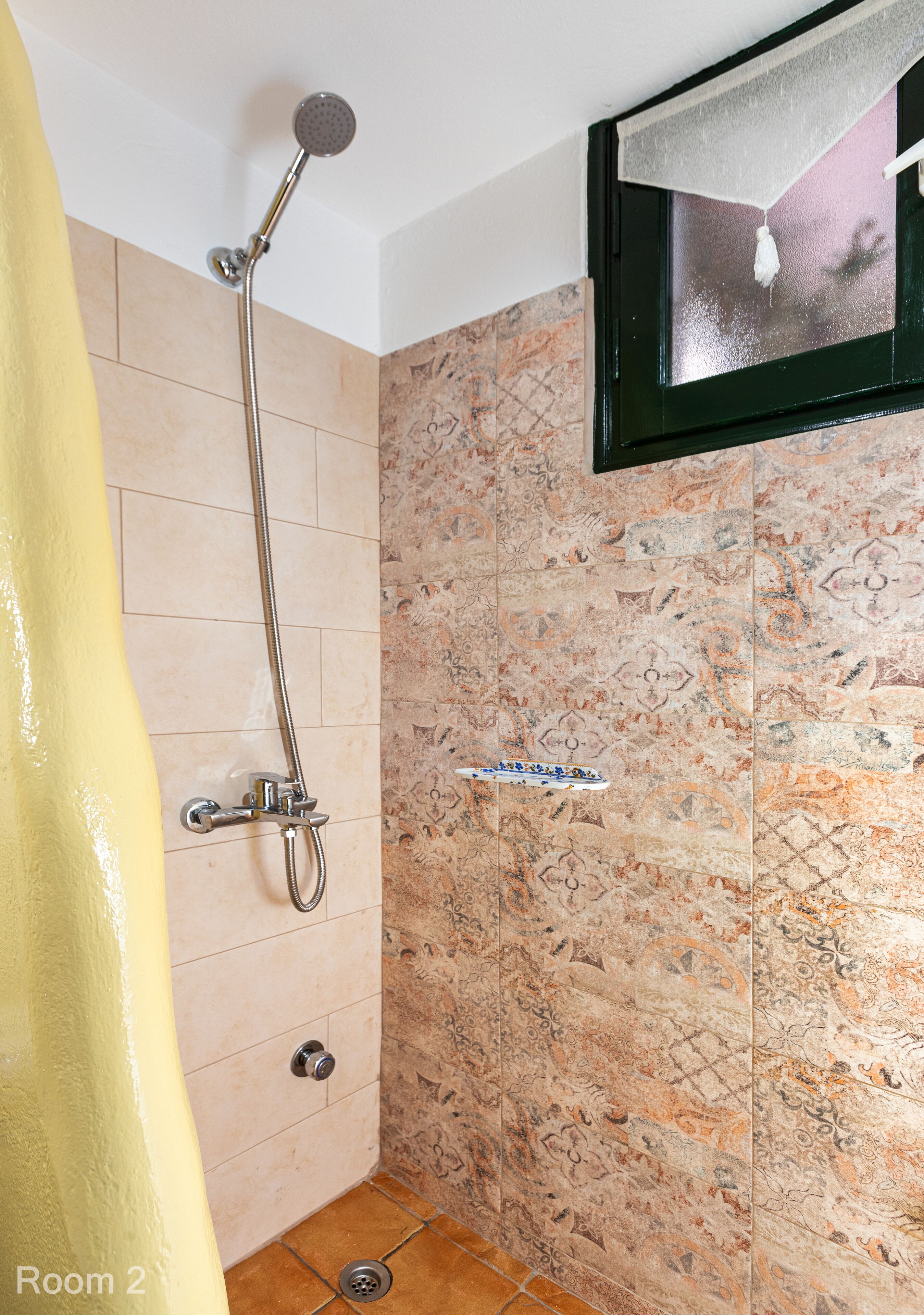 Um banheiro com chuveiro, paredes revestidas de azulejo, cortina amarela e uma prateleira pequena.