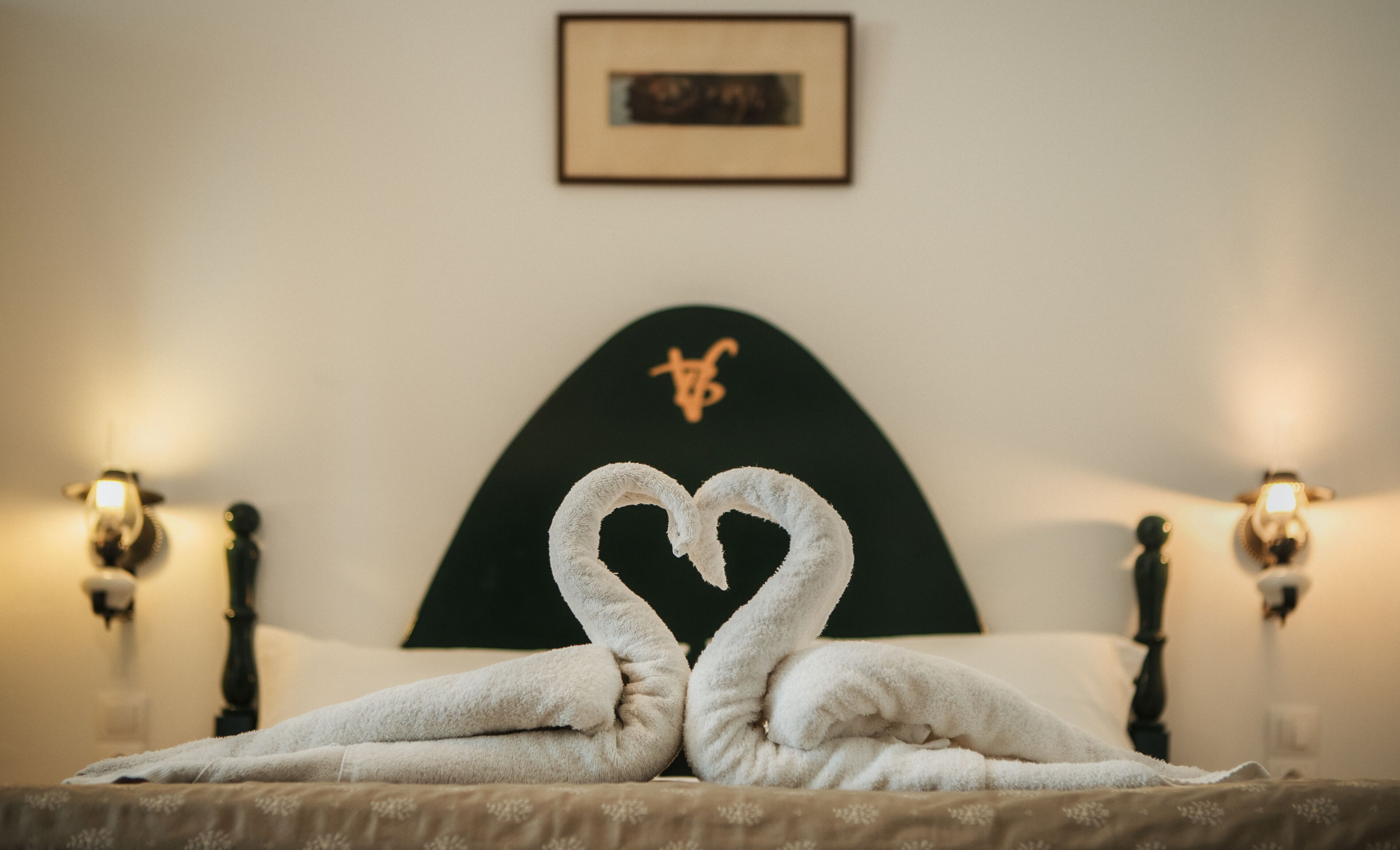 Una cama con una toalla dispuesta en forma de corazón y un cuadro en la pared.