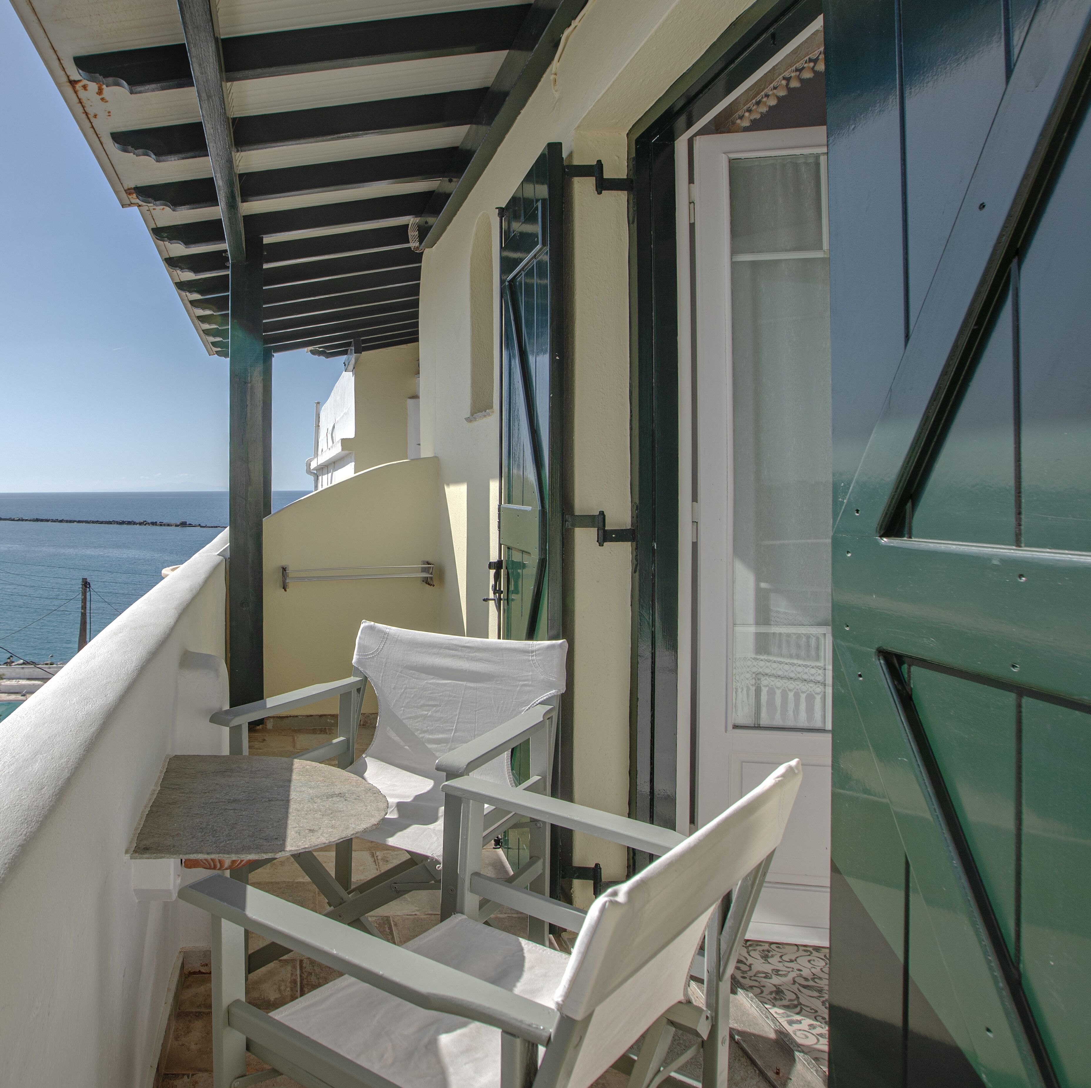 A balcony with a table and two chairs, overlooking the sea.