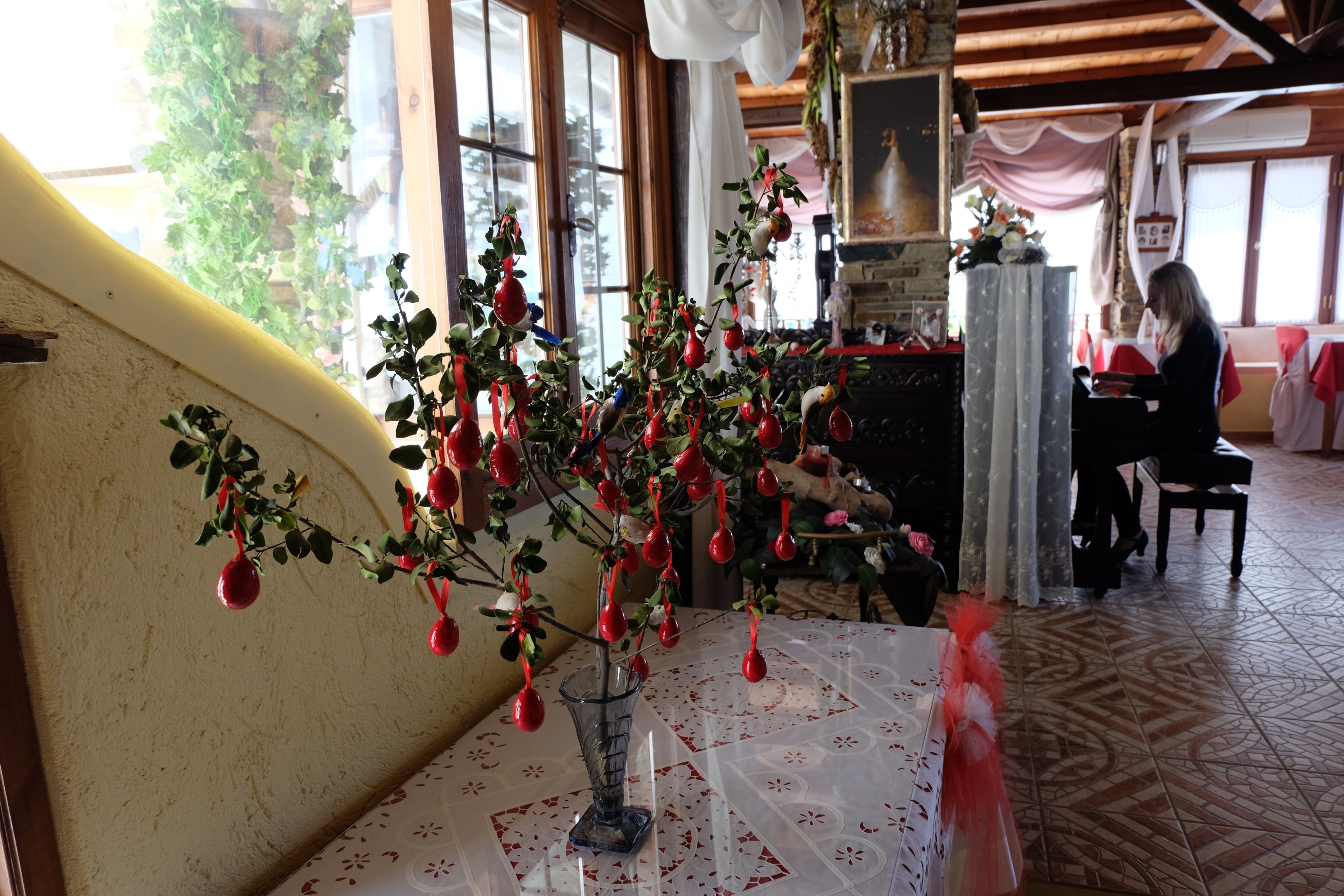 A room with a table featuring a glass vase with a plant and red ornaments. There is a window with a view of greenery outside.