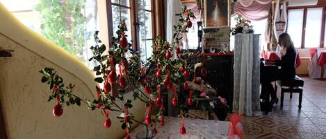 A room with a table featuring a glass vase with a plant and red ornaments. There is a window with a view of greenery outside.