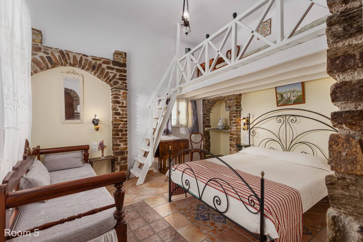 A bedroom with a wooden bed, a desk, and a chair. There is a staircase leading to an upper level.