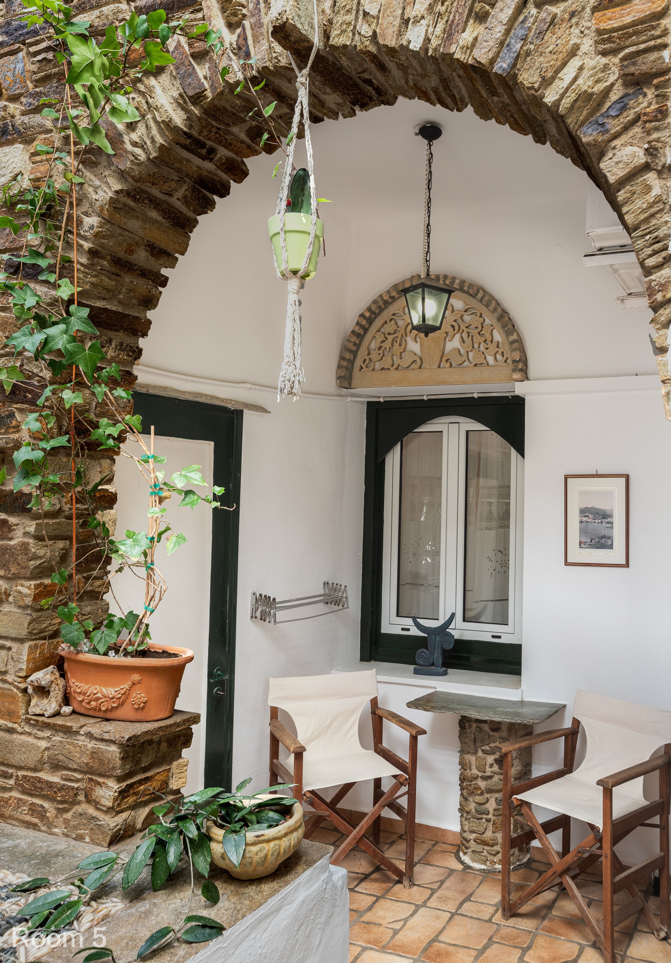 A room with a stone archway, a hanging planter, a table with chairs, and a window with a view.