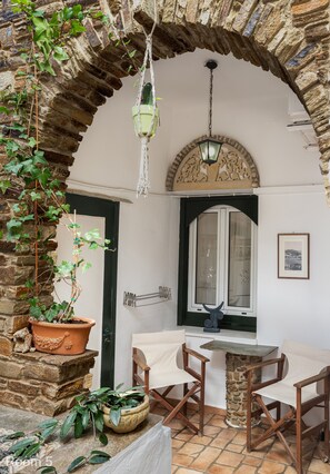 A room with a stone archway, a hanging planter, a table with chairs, and a window with a view. - Voreades (Tinos)