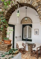 Una habitación con un arco de piedra, una planta colgante, una mesa con sillas y una ventana con vistas.