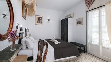 A bedroom with a large bed, a wooden chair, a desk with a vase of flowers, a mirror, and a wardrobe.