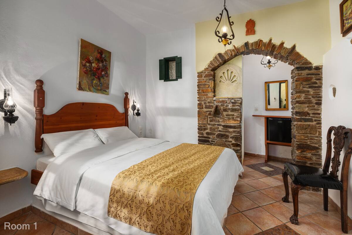 A bedroom with a wooden bed, a stone wall, a mirror, and a small table.