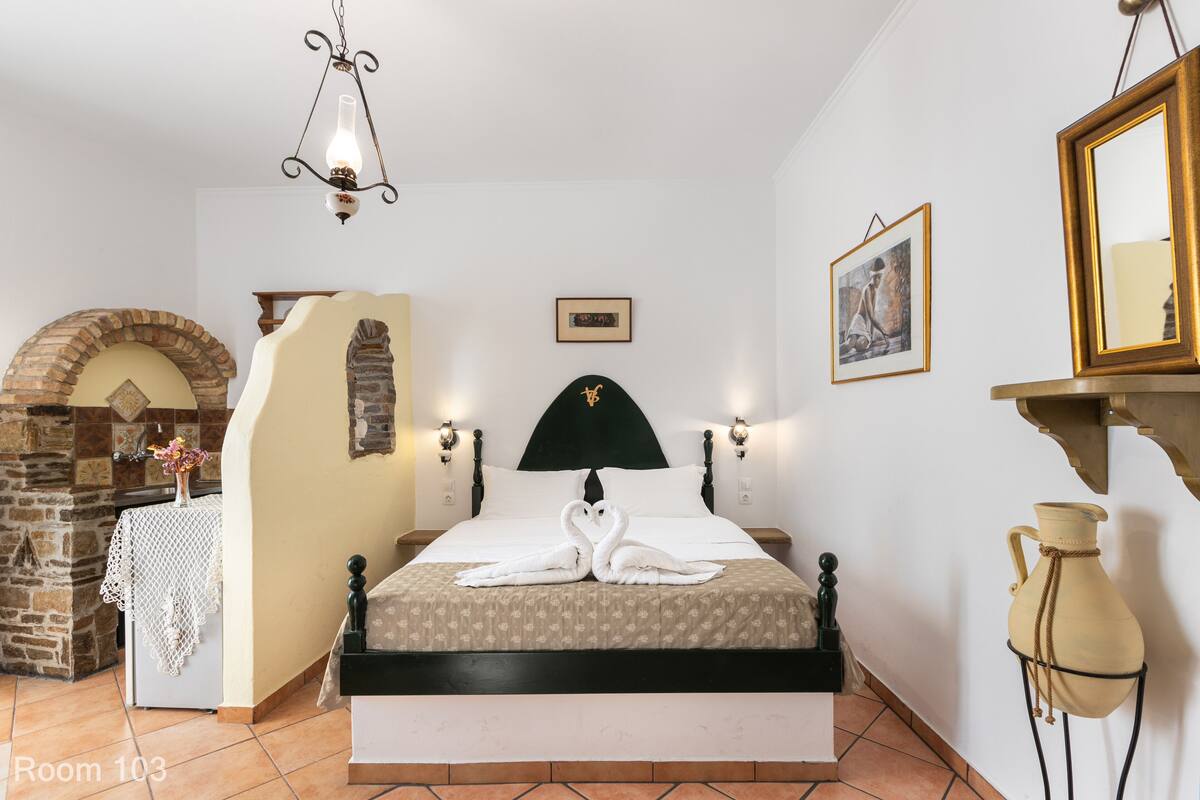 A neatly arranged bedroom with a bed centered, a stone fireplace, and a chandelier.