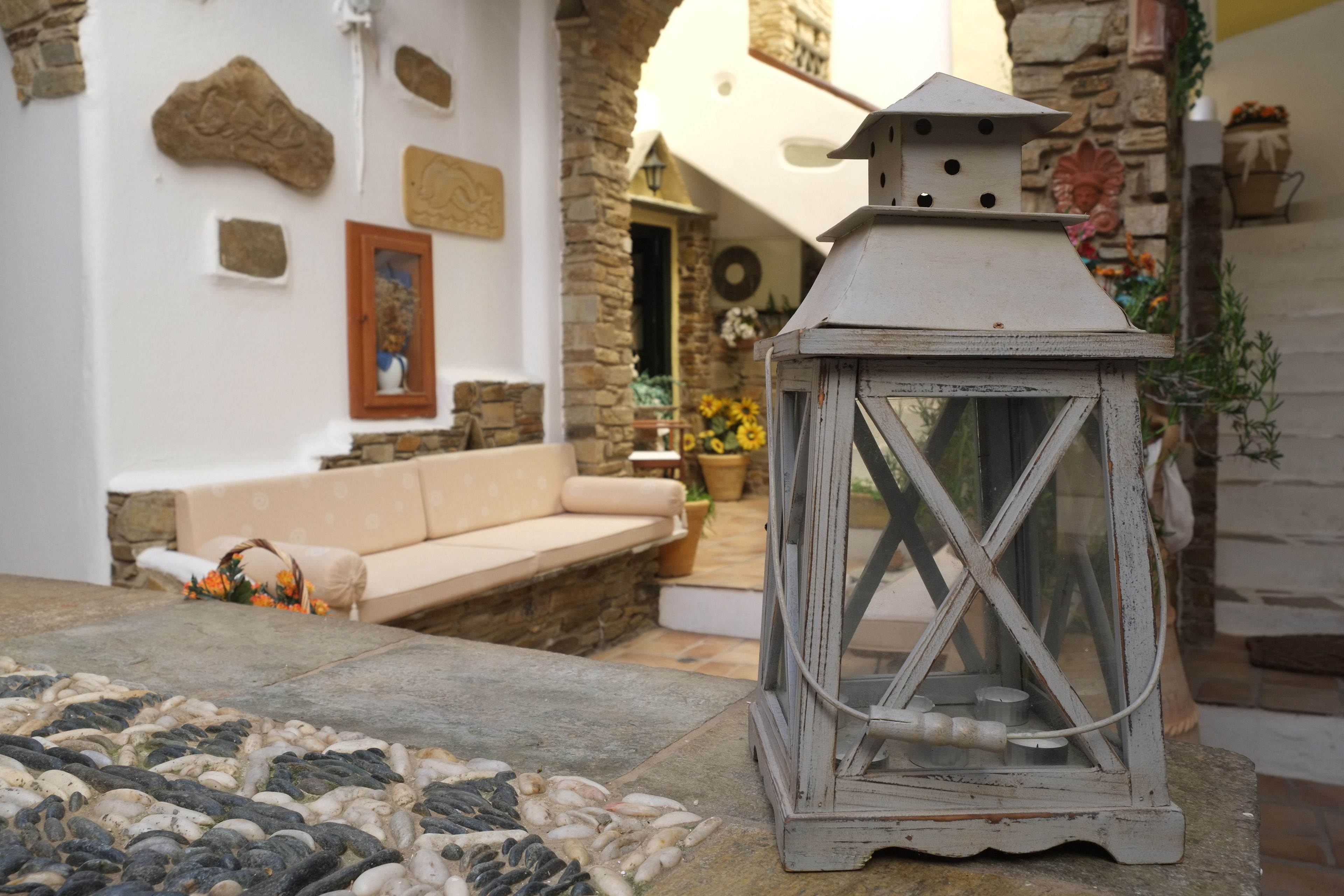 A stone-floored patio with a white lantern, a beige sofa, and a stone wall with decorative elements.