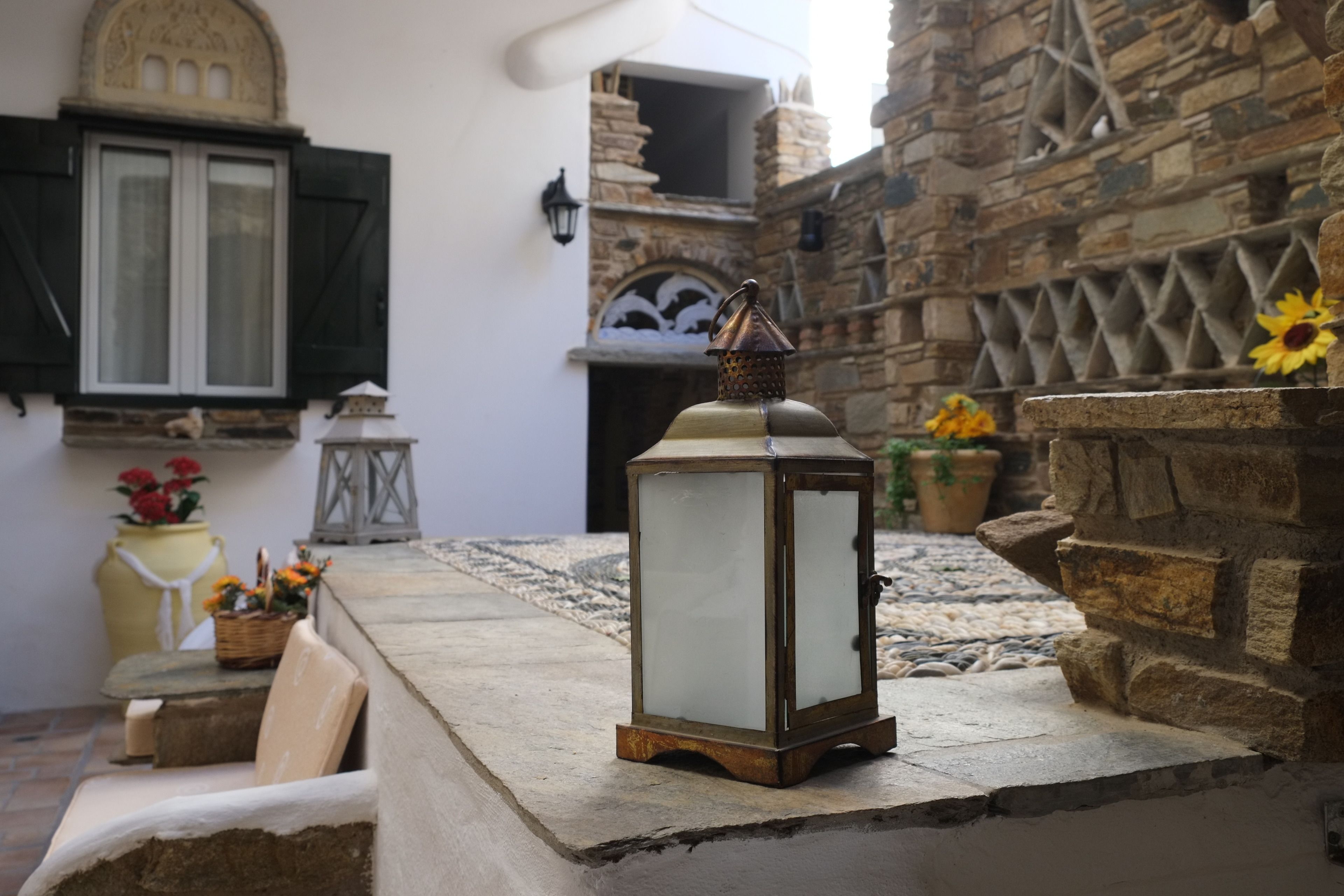 A stone wall with a lantern, a window with shutters, and a potted plant.