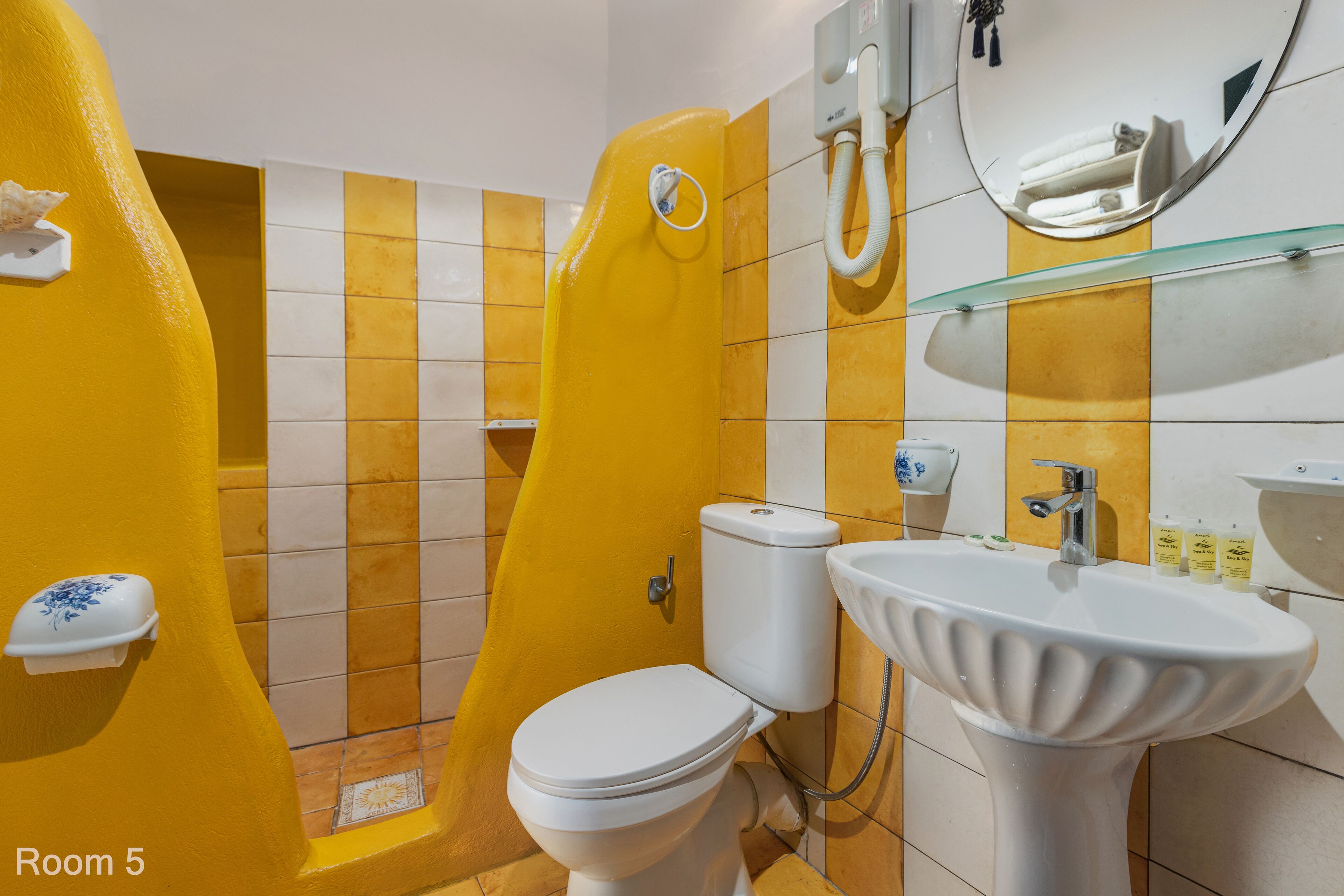 A bathroom with a yellow and white tiled wall, a white toilet, a sink, and a shower area.