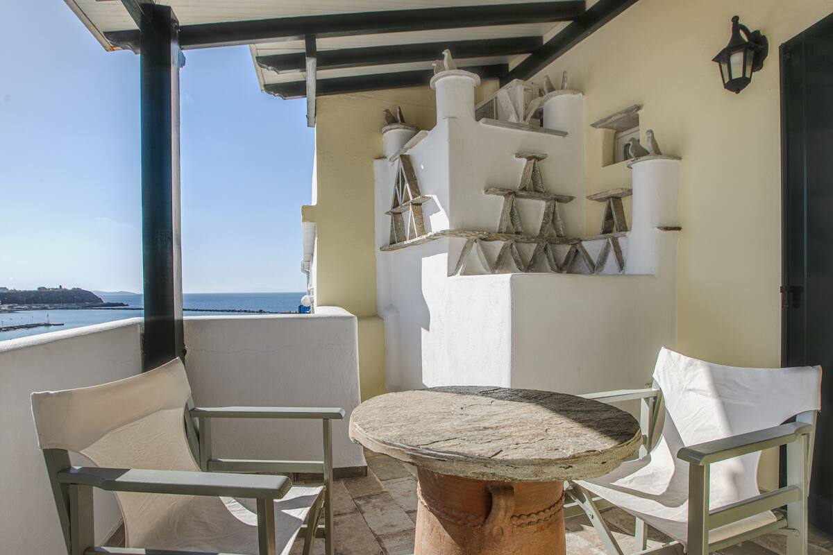 A balcony with white chairs, a round table, and a view of the sea.