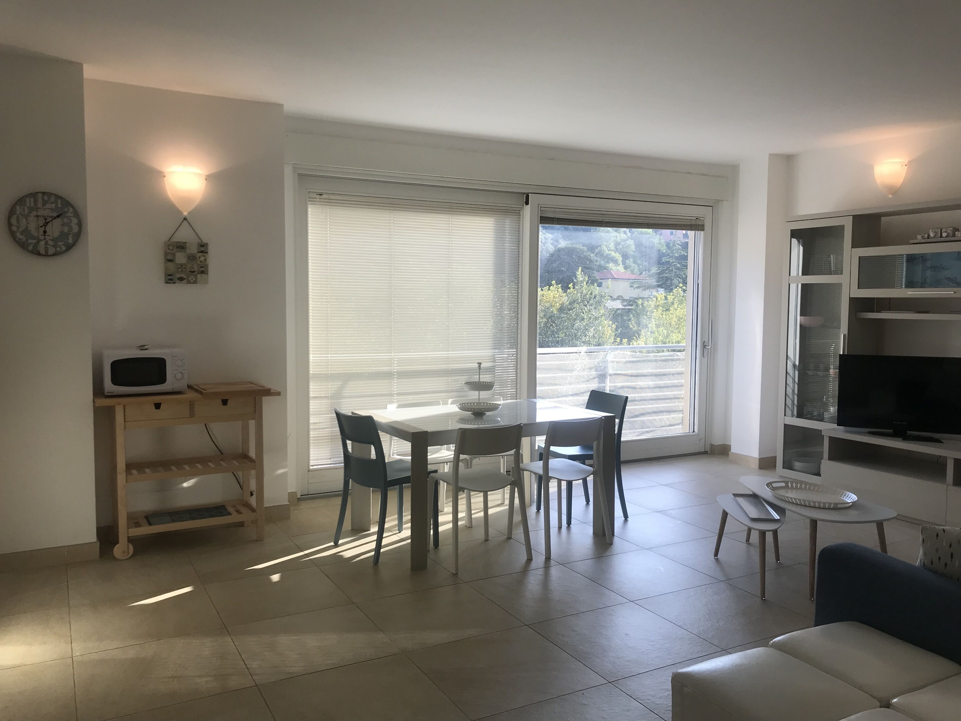 Una sala de estar moderna con comedor, televisor y balcón con vistas a zonas verdes.
