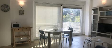 Una sala de estar moderna con comedor, televisor y balcón con vistas a zonas verdes.