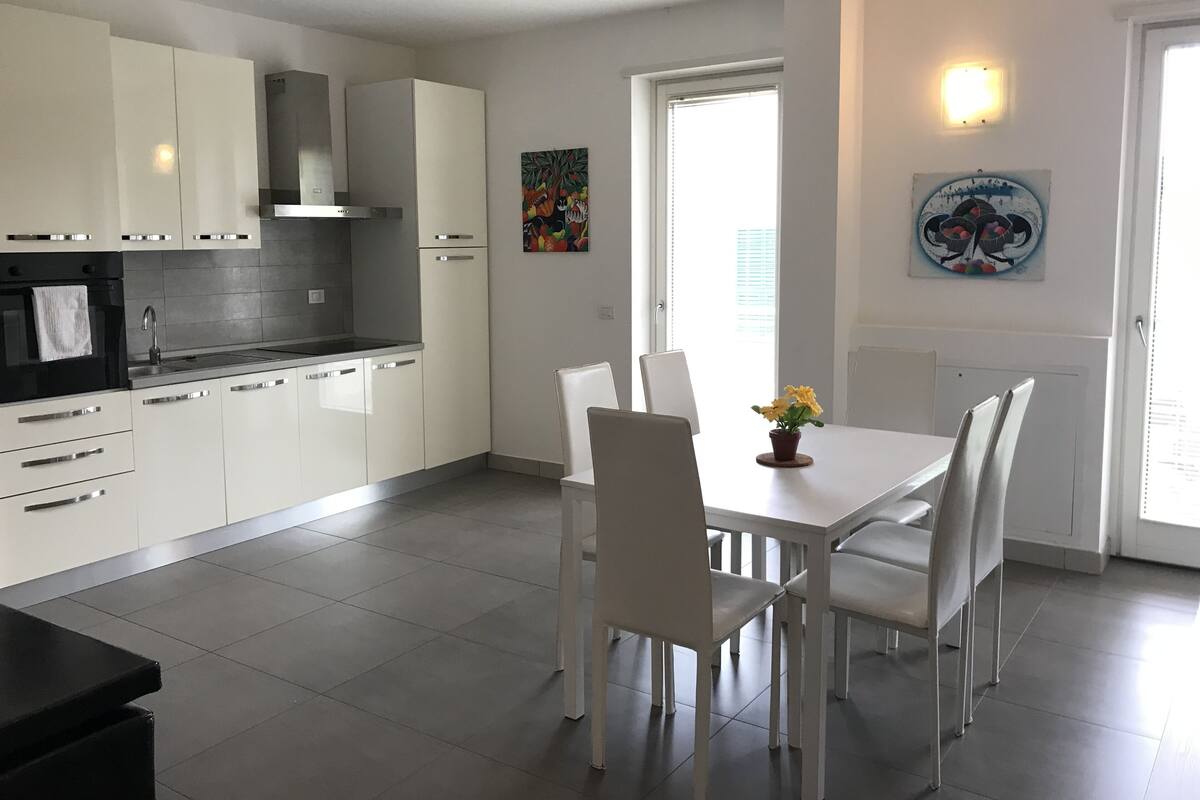 Une cuisine moderne avec des meubles blancs, une cuisinière noire et un coin repas comprenant une table et des chaises blanches.
