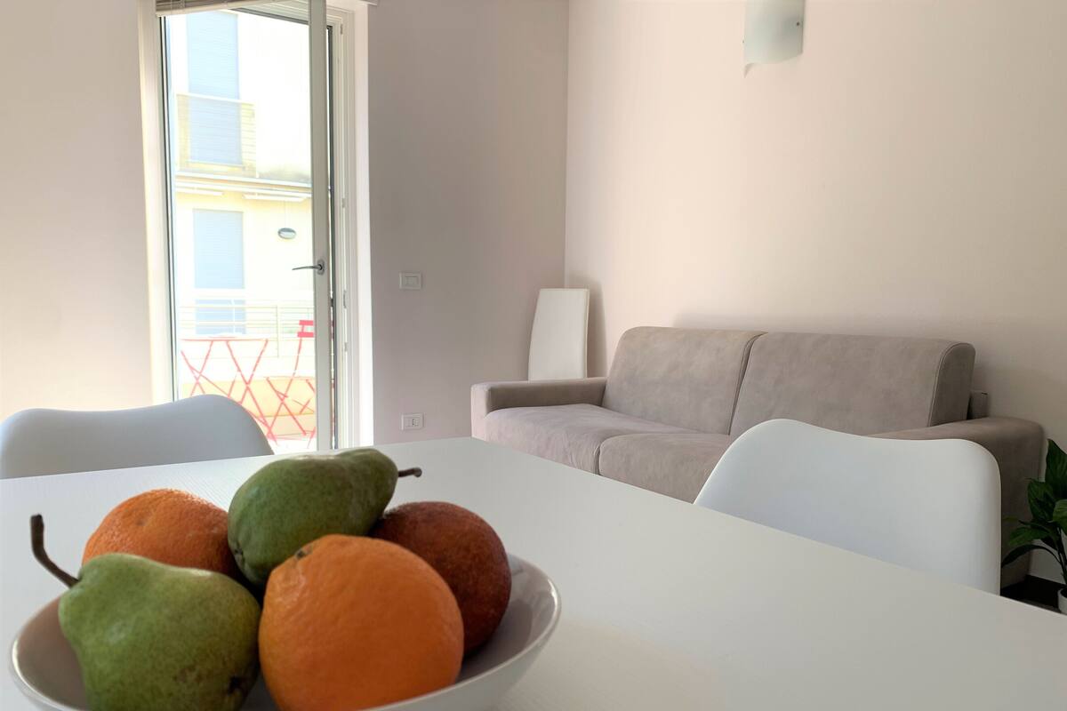 Une table à manger avec un saladier de fruits, un canapé et une vue sur l’extérieur.