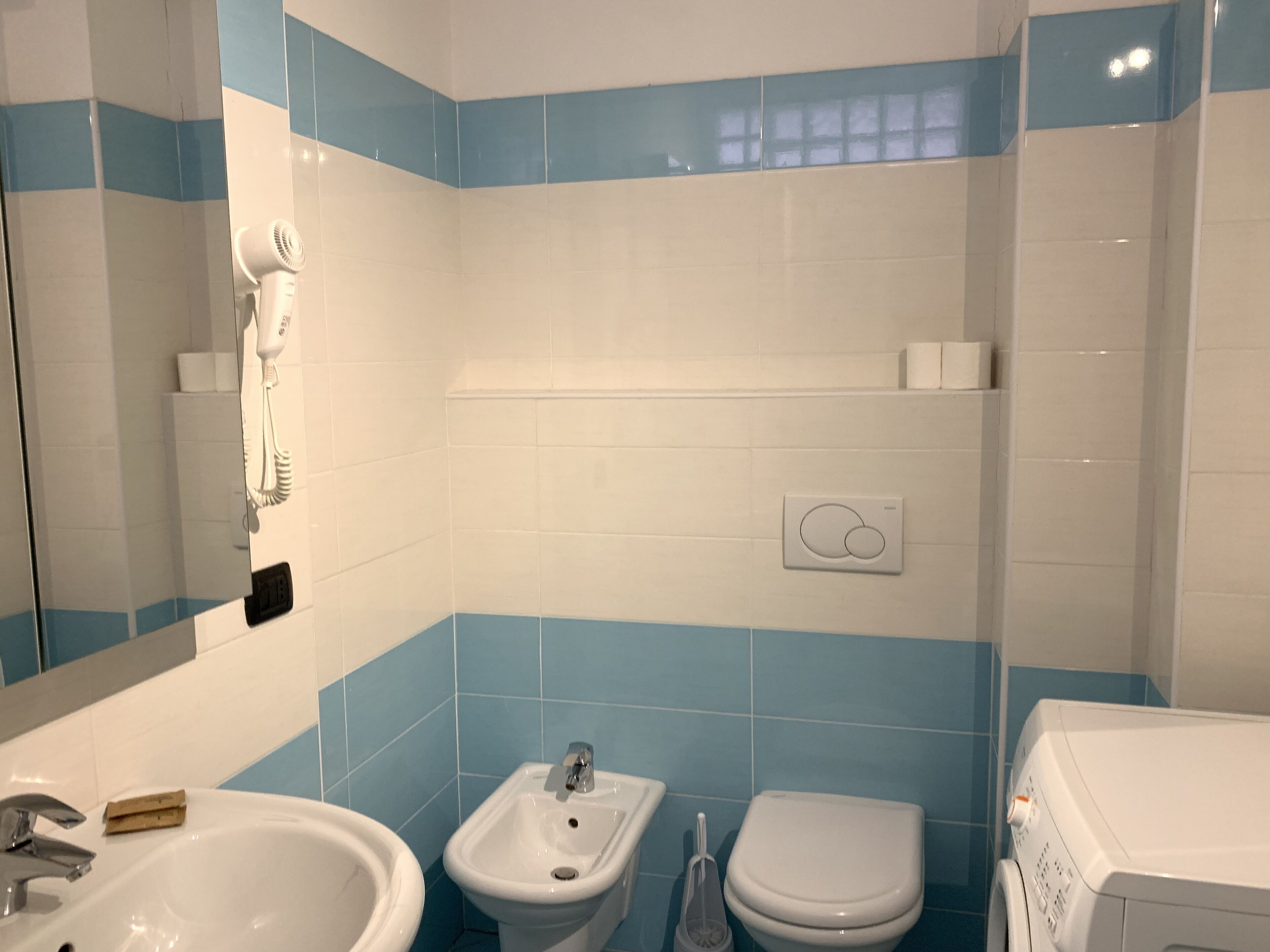 A bathroom with a sink, bidet, toilet, and a hairdryer mounted on the wall.